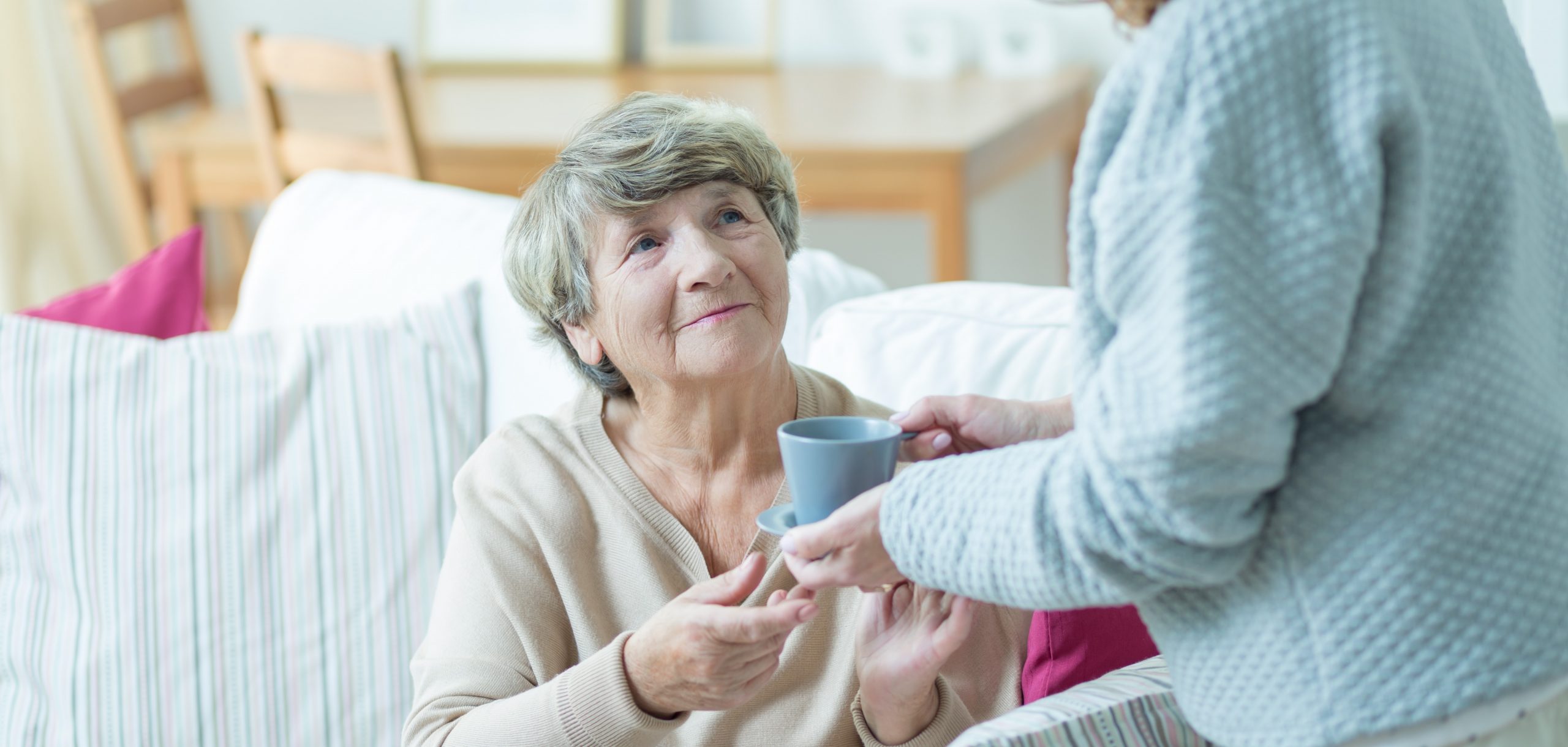 caregiver daughter giving a cup of tea to her mum