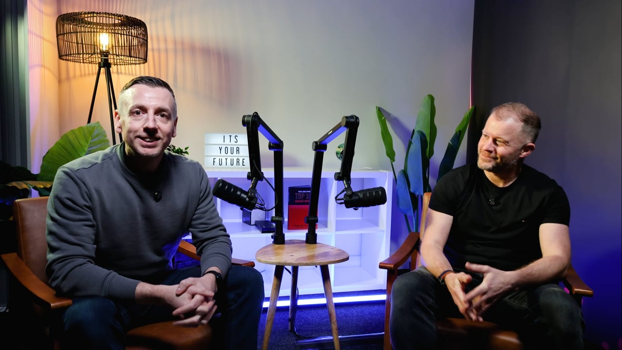 Darren and Wayne seated opposite one another in the studio with podcast microphones.